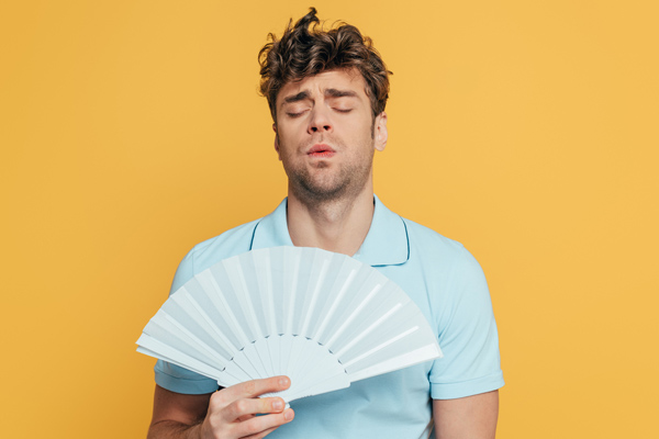 man cooling himself with a fan due to broken air conditioner