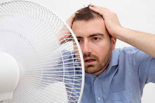 flushed man feeling hot in front of a fan due to poor heat pump performance