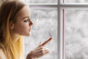 image of woman sitting by window in winter depicting air leakage