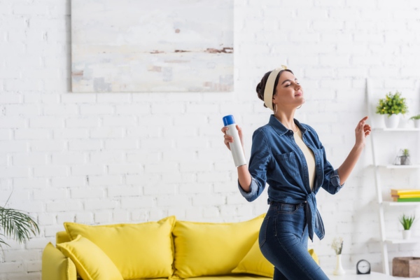 Woman holding bottle of aerosol air freshener at home